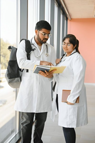 Two medical students in white lab coats discussing notes in a hallway, representing mbbs guidance and academic support.